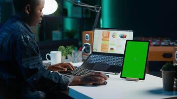 Freelancer using isolated screen tablet, analyzing statistical charts on laptop in living room. Remote employee checking business revenue numbers on chroma key electronic device video