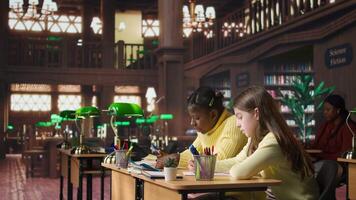 Diverse classmates scholars doing their class homework together in the library, working hard to obtain good grades. Focused schoolgirls solving their assignments with academic materials. Camera A. video