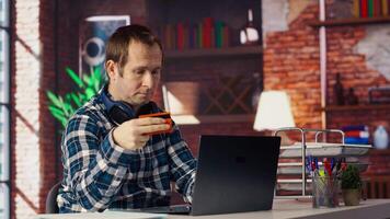 contento hombre emocionado a hacer en línea compras, mecanografía débito tarjeta información en ordenador portátil en departamento. alegre persona a escritorio utilizando computadora portátil, agregando pago método en sitio web, cámara si video