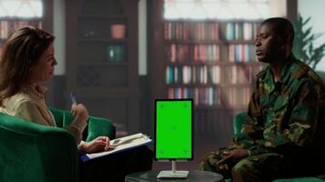 Infantry serviceman attending a therapy session with psychologist next to mockup display, suffering from PTSD after combat. Female counselor offers help and support to army officer. Camera B. video