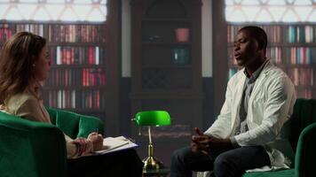 Black surgeon opening up about hard patient cases and PTSD, psychologist listens to advice in a counseling session. Doctor sharing feelings after losing people, trauma support. Camera B. video