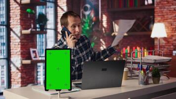 Chroma key tablet next to freelancer in home office sitting at desk in front of laptop, answering phone call. Isolated screen device next to freelancer receiving telephone call on smartphone, camera A video