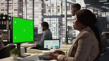 Female director seated at workstation with green screen on devices, working on solving administrative tasks for enterprise growth. Performance metrics to support project objectives. Camera B. video