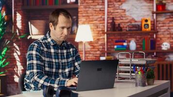Man seated at home office desk using laptop, checking emails displayed on screen, reading messages in inbox, composing and sending replies, managing electronic correspondence, camera B video