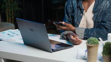 African american teleworker receiving phone call from job colleague while working from home on laptop. Freelancer speaking with coworker using smartphone while solving tasks, camera A video