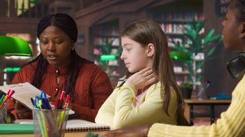 African american professor mentoring diverse schoolgirls in the library, learning together in a library filled with curriculum based materials. Woman tutoring pupils on literature. Camera A. video