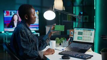 Woman taking break from checking stock exchange to watch videos on green screen smartphone. Stockholder working from home using chroma key phone and looking at market shares growth