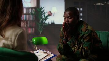 Black armed forces warrior faces trauma and anxiety at counseling session, addressing PTSD and talking about horror war scenes. Distraught trooper shares war flashbacks. Camera A. video