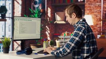 Man in home office stretches back while looking at UI on PC screen, feeling fatigued while executing programming code. IT developer feeling backpain, relieving pain, writing and testing code, camera B video