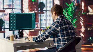 Man seated at desk using AI LLM chatbot software in modern urban home office. Person requesting help from large language model program on computer in bright apartment workspace, camera B video