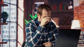 Stressed man in home office scratching head with pen, upset after having to answer too many emails on laptop. Fatigued teleworker feeling overworked by too many project tasks, camera B video