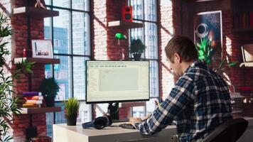 Man in home office looking at UI on PC screen, typing and executing programming code. Coding application UI used by IT developer writing and testing code in modern workspace, camera A video