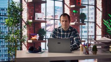 Man seated at home office desk using laptop, answering phone call while checking emails displayed on screen. Worker in telephone call with friend at work while reading messages in inbox, camera A video