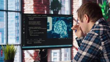 Admin uses computer for artificial intelligence computing simulation, waiting for code to finish compiling. Man works with AI deep neural networks, rubbing forehead with pen, feeling bored, camera A video