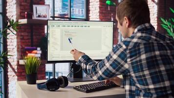 Programmer at desk types code into computer, developing software programs, entering commands. Man at home fixing errors in application, implementing new features pointing to code with pen, camera A video