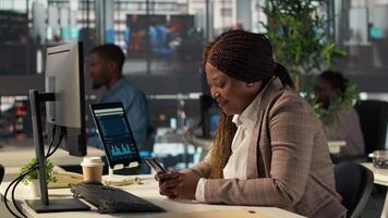 Black business employee browses social media webpages on her phone, taking a short break to answer a few texts at the office. Female worker does online communication via texting. Camera A. video