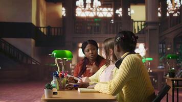 Preteens girls and their professor collaborating on schoolwork at the library, focused on academic materials to write a good essay. Students collect extra information with private lessons. Camera A. video