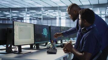 Data center manager helps intern implement AI predictive maintenance systems. Server farm supervisor checks work done by employee using artificial intelligence to identify hardware failures, camera A video