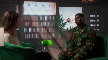 Female psychologist assists a black soldier in a counseling session, focusing on PTSD and trauma after combat distress. Mental health support for army veterans, grief and guilt. Camera A. video