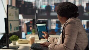 Confident businesswoman at her office desk working on report writing and answering emails, administrative tasks management. Black female expert reviewing objectives to ensure success. Camera A. video