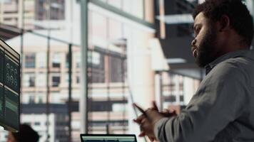 Black male CEO dealing with back pain and stretching his muscles at the desk, sitting with an incorrect posture and trying to fix it. General manager working with data analytics. Camera A. video