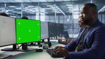African american data center admin using mockup PC, maintaining company network infrastructure. Man working in server farm ensuring optimal system performance with green screen computer video
