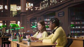 African american private teacher offering support to her students, tutoring them through a lesson plan at a library desk. Tutor providing learning materials, mentoring scholars. Camera A. video
