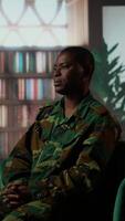 Vertical African american serviceman in camouflage uniform sits in therapy, looking depressed and opening up about combat scenes. War veteran soldier dealing with PTSD, reintegration program. Camera B. video