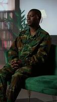 Vertical African american serviceman in camouflage uniform sits in therapy, looking depressed and opening up about combat scenes. War veteran soldier dealing with PTSD, reintegration program. Camera A. video