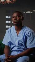 Vertical African american nurse struggles with depersonalization condition due to work PTSD, dealing with derealization and being in a dissociative state. Assistant at the hospital has anxiety. Camera A. video