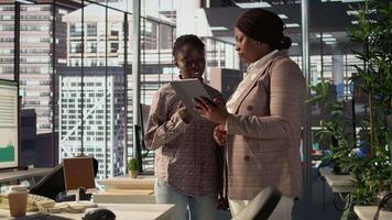 Black manager reviews company strategy with her female assistant in a high end corporate office, making key business decisions to support organizational growth. Discuss resource allocation. Camera B. video