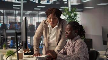 Female employee and manager gathered around a workstation discussing objectives and strategizing solutions to solve administrative tasks faster. Aligning business goals and milestones. Camera B. video