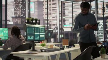 Black analyst working with monthly revenue balance to create financial plans using online tools, analyzing data infographics. Businessman managing organizational goals for efficiency. Camera B. video