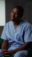 Vertical African american medical assistant in scrubs reflects on loss and burnout, sharing his feelings and anxiety based on career stress trauma. Emotional support and post traumatic healing. Camera B. video