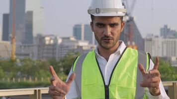 Engineer in a white helmet and high-visibility vest holding a tablet, gesturing confidently outdoors. Urban skyline and construction cranes in the background symbolize modern infrastructure. video