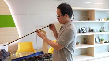Man practicing violin indoors near a bright window, surrounded by minimalist decor and greenery. The scene captures a peaceful moment of musical focus and dedication to art. video