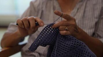 Elderly woman knitting in a cozy room, focused on creating a beautiful piece with blue yarn. A serene moment showcasing craftsmanship, creativity, and the joy of handmade art. video