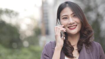 Elegant woman in a purple blazer using her smartphone, gracefully waving in a modern outdoor setting. A blend of style, technology, and sophistication with a warm and cheerful expression. video