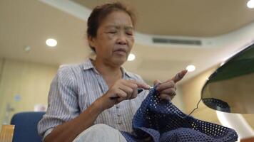 Elderly woman knitting in a cozy room, focused on creating a beautiful piece with blue yarn. A serene moment showcasing craftsmanship, creativity, and the joy of handmade art. video