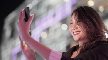 Elegant woman in a purple blazer using her smartphone, gracefully waving in a modern outdoor setting. A blend of style, technology, and sophistication with a warm and cheerful expression. video