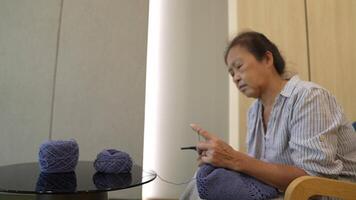 Elderly woman knitting in a cozy room, focused on creating a beautiful piece with blue yarn. A serene moment showcasing craftsmanship, creativity, and the joy of handmade art. video