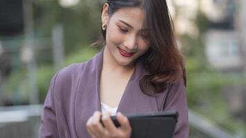 Elegant woman in a purple blazer using her smartphone, gracefully waving in a modern outdoor setting. A blend of style, technology, and sophistication with a warm and cheerful expression. video