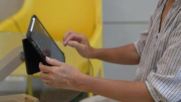 Senior woman using a smartphone near a large window with urban greenery outside, focusing intently on the screen. A scene blending modern technology with serene surroundings. video