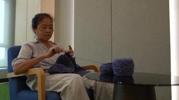 Elderly woman knitting in a cozy room, focused on creating a beautiful piece with blue yarn. A serene moment showcasing craftsmanship, creativity, and the joy of handmade art. video