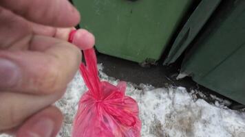 An individual is walking on a snowy ground while holding a bright red bag. Distinctive tire tracks are clearly visible in the snow, indicating some level of activity in the local area video