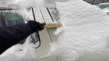 A person is diligently removing a thick layer of snow from a cars windshield, which highlights the significant challenges and difficulties faced during winter driving in an urban setting video