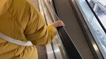 A cozy yellow jacketclad arm is gently resting on the smooth escalator rail, while a stunning and picturesque scenic outdoor view unfolds right through the large nearby glass windows video