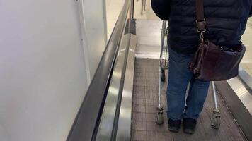 A lone person skillfully maneuvers a luggage cart on a moving walkway through a bustling shopping area, illuminated by bright lights and modern architecture, enhancing the experience video