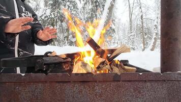 A person is warming their chilly hands by a cozy campfire in a picturesque snowy landscape, beautifully showcasing the joy and comfort of outdoor adventures in a serene winter scene video