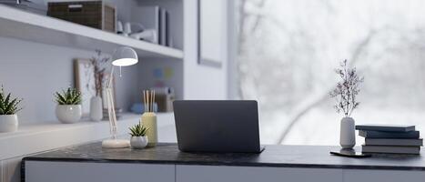 A back view of a laptop, a table lamp, and decor on a table in a modern home office workspace. photo